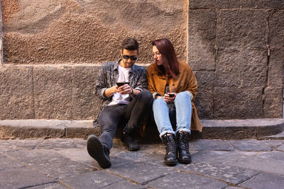 Full length of young man with woman holding wineglass against wall