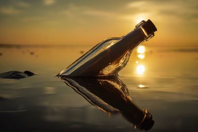 Close-up of bottle floating on water against sunset sky