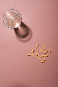 Group of yellow pills and glass of water on a pink background, top view