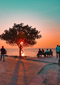 People riding bicycle on beach against sky during sunset