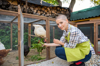 Portrait of woman feeding hen in chicken coop