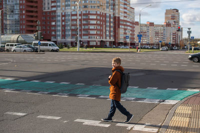 A boy with a backpack crosses the road at a pedestrian crossing