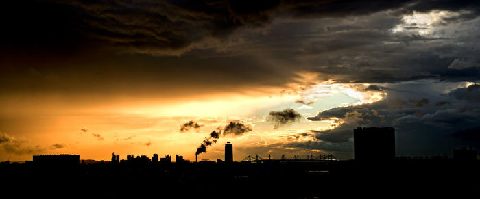 Silhouette of factory against sky during sunset