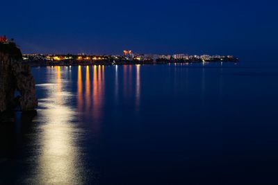 Illuminated city by sea against clear sky at night