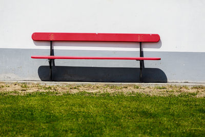 Empty bench on field against wall
