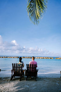 Rear view of people sitting on beach against sky