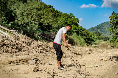 Side view of man cutting wood while standing on ground