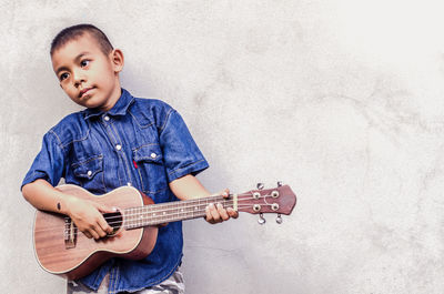 Boy playing guitar against wall