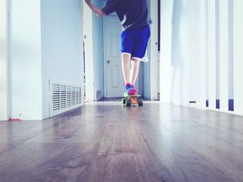 Low section of boy skateboarding on hardwood floor at home