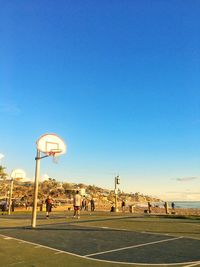 People playing basketball court against clear blue sky