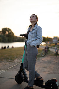 Young woman looking away while standing on push scooter against sky