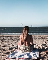 Rear view of woman sitting at beach on sunny day