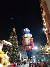 People at illuminated christmas lights against sky at night