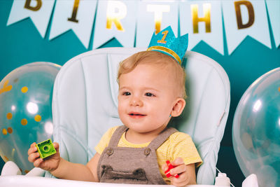 Close-up of cute baby boy sitting on high chair in birthday party