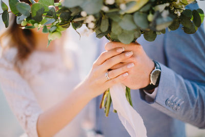 Midsection of bride and groom holding bouquet