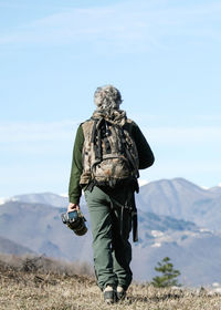 Rear view of man walking on field against sky