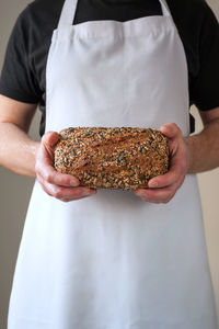 Midsection shoot, bakers hands holding  loaf of organic sourdough wholegrain bread in front of him.