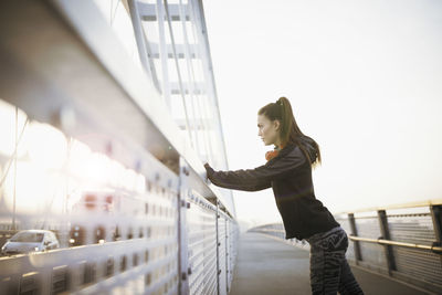 Side view of young woman standing against railing