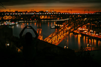 Rear view of illuminated bridge over river against sky at night