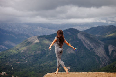 Rear view full length of woman exercising on cliff against sky