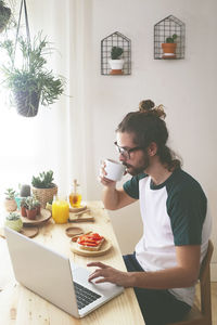 Young man using laptop while having breakfast