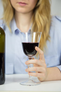 Midsection of woman holding wine bottle and wineglass over white background