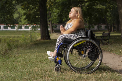 Young woman with short height on wheelchair meditates, relaxing in green park at summer day. full