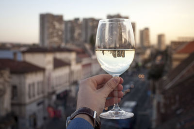 Cropped hand of businessman holding wine in glass against city