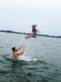 Shirtless father throwing daughter while standing in sea against sky
