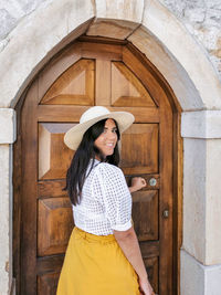 Happy young woman smiling as she's opening door of a house.