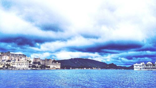 City at waterfront against cloudy sky