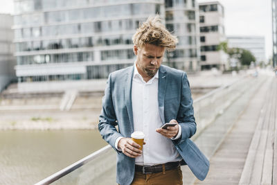 Businessman with cell phone and coffee to go on bridge