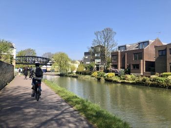People riding bicycle on canal amidst buildings in city