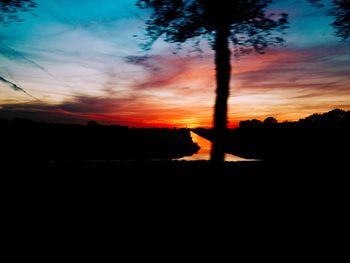 Silhouette trees on field against orange sky