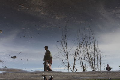 Reflection of man and woman reflecting on water at beach 