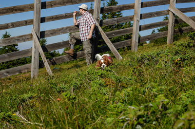 Farmer leaned on a wooden fence and his dog