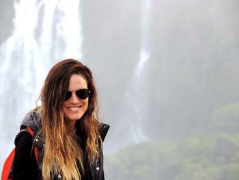 Smiling woman standing against waterfall