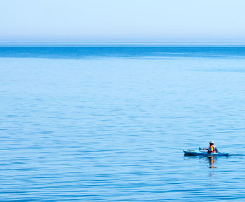 Person kayaking in sea against clear sky