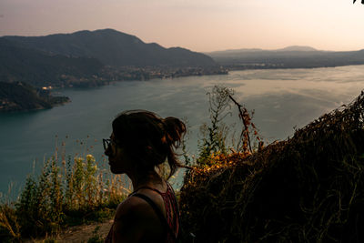 Side view of woman looking at sea while standing on mountain against sky