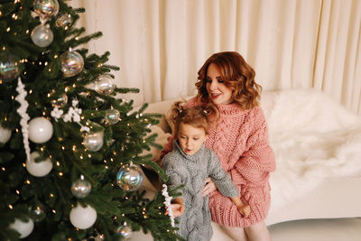 Happy mom and little daughter kid in sweaters hugging getting ready for  christmas holiday at home