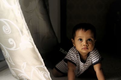 Cute baby boy crawling by curtain at home