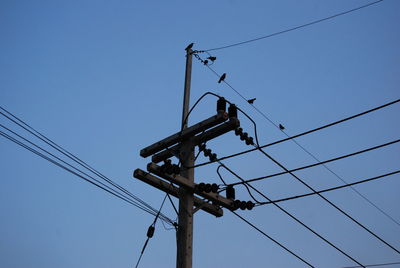 Low angle view of electricity pylon against clear blue sky
