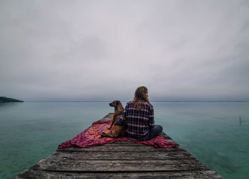 Rear view of woman with dog sitting on pier over lake