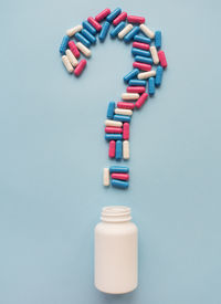 High angle view of pills spilling from bottle against pink background