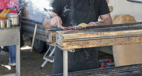 Midsection of male vendor cooking meat on barbecue at market