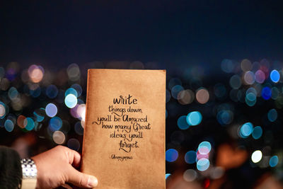 Midsection of person holding illuminated text at night