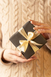 A box with a gift wrapped in brown paper and tied with a gold ribbon, in female hands, close-up