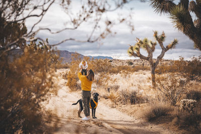 A woman with a baby and a dog is standing in a desert of california