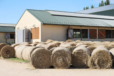 Hay bales on field by building against clear sky