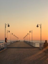 Street lights on pier over sea against clear sky during sunset